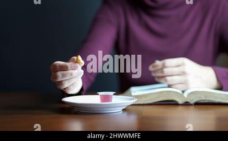 Femme tenant un morceau de biscuit avec une tasse de vin sur la table. Prendre le concept de Sainte Communion chrétienne. Banque D'Images