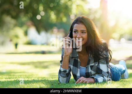 Je suis en attente dans le parc. Photo d'une jeune femme attirante parlant au téléphone dans un parc. Banque D'Images