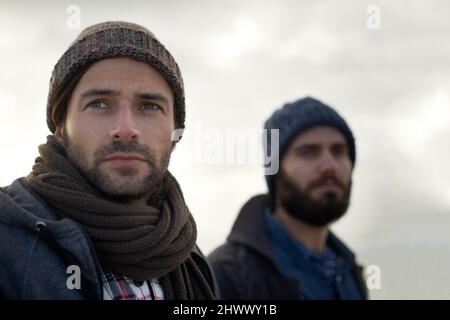 Enveloppé dans le froid de l'océan. Deux beaux jeunes pêcheurs se tenant sur la plage un matin frais. Banque D'Images