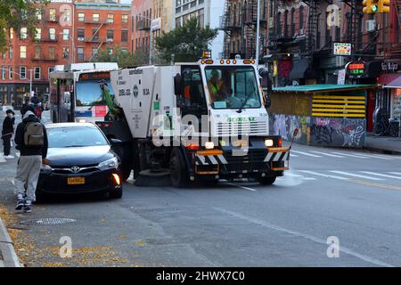 Un balai de rue New York Sanitation manœuvrant autour d'une « voiture noire » à l'écart du trottoir, bloquant Essex St dans le Lower East Side Banque D'Images