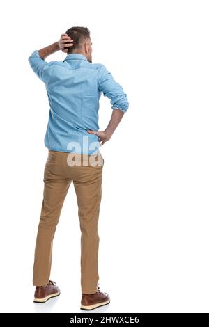 vue arrière d'un jeune homme confus dans une chemise en denim qui se gratte la tête et pense à quelques problèmes difficiles sur fond blanc Banque D'Images