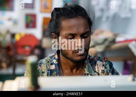 Jeune designer contemporain de vêtements assis devant une machine à coudre électrique et travaillant sur une nouvelle collection de mode Banque D'Images