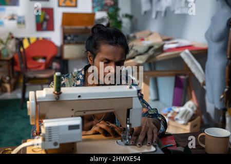 Jeune créateur de mode créatif se pencher sur la machine à coudre électrique et créer une nouvelle collection saisonnière dans l'atelier Banque D'Images