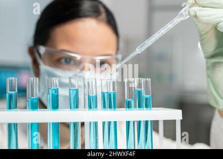 Partie du visage de la jeune femme travaillant en laboratoire dans un masque de protection et des lunettes mélangeant deux substances chimiques Banque D'Images