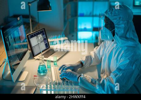 Scientifique afro-américain contemporain dactylographiant sur clavier d'ordinateur tout en analysant les résultats de l'expérience scientifique en laboratoire Banque D'Images