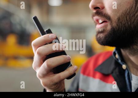 Main de l'employé barbu de l'usine parlant dans un émetteur-récepteur radio portable tout en donnant des instructions aux subordonnés de l'entrepôt Banque D'Images