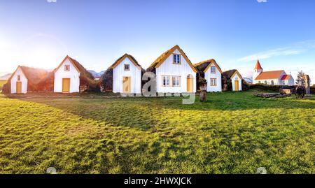 Maisons traditionnelles en toiture d'herbe de Glaumbaer, nord-ouest de l'Islande, avec une église en toile de fond rouge. Panorama en fin d'après-midi sous le soleil. Banque D'Images