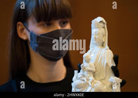 Un membre du personnel du British Museum regarde une figure de porcelaine de Guanyin avec des enfants et des préposés, de Chine, 18th siècle, lors du lancement de l'exposition Citi puissance féminine: Le divin au démoniaque, à l'occasion de la Journée internationale de la femme au British Museum de Londres, pour le dévoilement d'une icône nouvellement acquise de la déesse hindoue Kali par l'artiste bengali Kaushik Ghosh. Date de la photo: Mardi 8 mars 2022. Banque D'Images