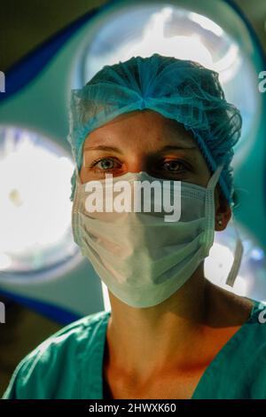 Une femme chirurgien regarde directement la caméra depuis le dessous des lampes chirurgicales (MODÈLE RELÂCHÉ) Banque D'Images