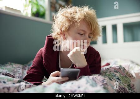 Adolescente malheureuse couché sur le lit à la maison Withg téléphone mobile victime d'intimidation sur les médias sociaux Banque D'Images