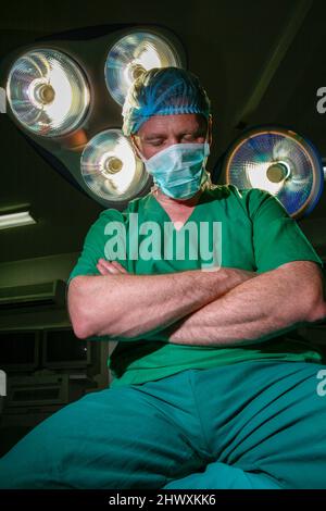 Le chirurgien fatigué est assis sur une table d'opération avec les bras pliés (MODÈLE RELÂCHÉ) Banque D'Images