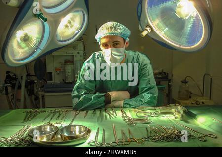 Un chirurgien masqué penche sur une rangée d'outils chirurgicaux stériles dans un théâtre d'hôpital (MODÈLE RELÂCHÉ) Banque D'Images