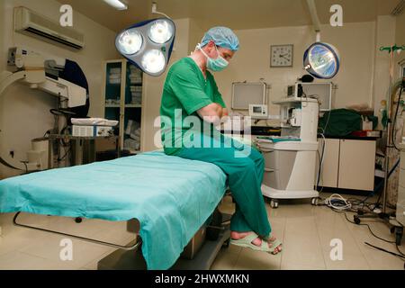 Un chirurgien fatigué s'assoit et dort sur une table d'opération. (MODÈLE DISPONIBLE) Banque D'Images