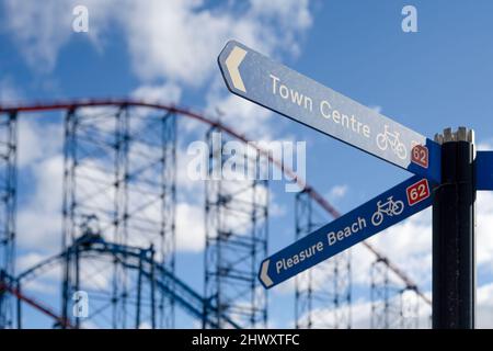 Un panneau de direction indiquant le chemin vers Pleasure Beach et le centre-ville de Blackpool, Lancashire, Royaume-Uni. Le rollercoaster « Big One » est en arrière-plan Banque D'Images