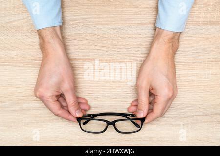 Mains tenant des lunettes. Sélection des lunettes, test oculaire, examen de la vision. Vue de dessus, plan d'appartement Banque D'Images