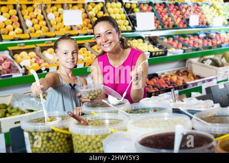 Bonne mère avec une fille prenant des olives savoureuses dans un contenant Banque D'Images