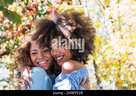 Gros plan de deux amies afro-américaines heureuses qui s'embrasent et rient dans le parc. Joyeux amis noirs afro avec des cheveux bouclés souriants Banque D'Images