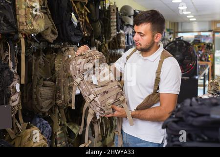 Homme choisissant un pistolet à sac à dos en textile dans un magasin militaire Banque D'Images