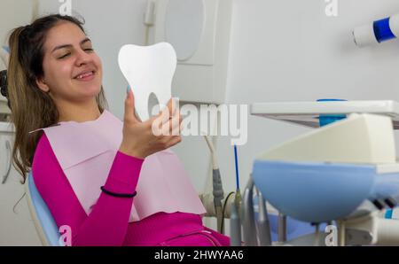 Une adolescente regarde ses bretelles et ses dents dans le miroir du cabinet du dentiste Banque D'Images