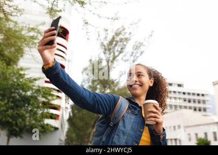 Bonne femme afro-américaine prenant selfie sur smartphone avec une tasse à café jetable Banque D'Images