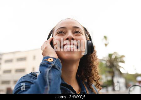 Bonne jeune femme afro-américaine à écouter de la musique à travers des écouteurs dans la ville Banque D'Images