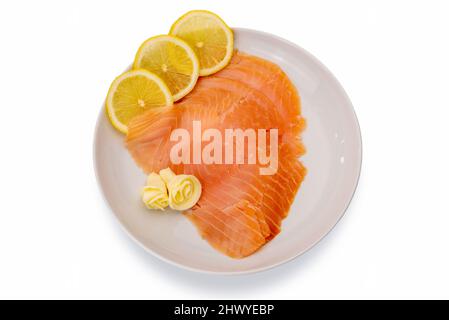 Tranches de saumon fumé avec des tranches de citron et des roses de beurre dans un plat blanc isolé sur fond blanc, vue du dessus, plat, passe-cheveux Banque D'Images