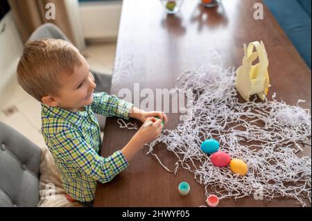 Un petit enfant peint des œufs de Pâques dans la cuisine Banque D'Images