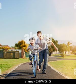 Aucune roue d'entraînement n'est nécessaire. Photo d'un père enseignant à son petit fils comment faire un vélo dans le parc. Banque D'Images