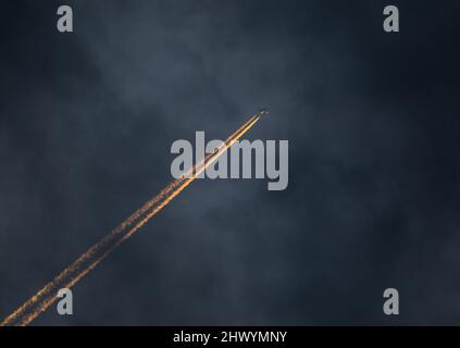 Un avion de ligne commercial à haute altitude vole au coucher du soleil avec des contrails éclairés. Banque D'Images