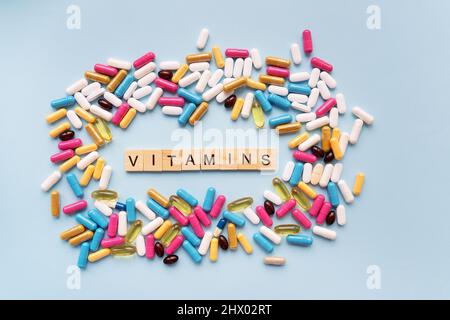 Beaucoup de comprimés lumineux multicolores, au centre il y a une inscription vitamines. Arrière-plan bleu. Concepts de médecine et de santé Banque D'Images