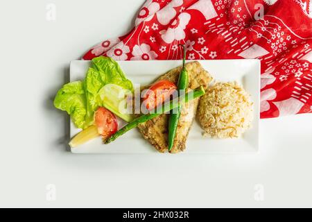 Bar de mer grillé avec riz et salade grecque dans un plat isolé sur table en toile colorée vue sur fond gris Banque D'Images