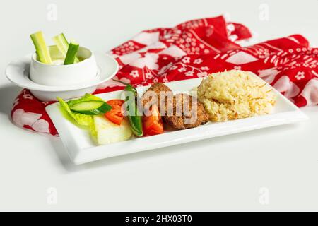 Cuisine turque traditionnelle riz Izgara Kofte wuth, raita et salade dans un plat isolé sur table en tissu coloré vue de dessus sur fond gris Banque D'Images