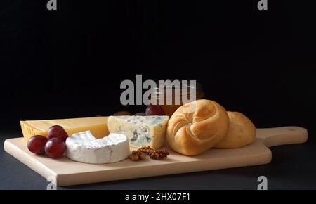 Délicieux plateau de fromages composé de camembert naturel, bleu et parmesan, garni de raisins bleus, noix, petits pains de blé et miel sont disposés sur Banque D'Images