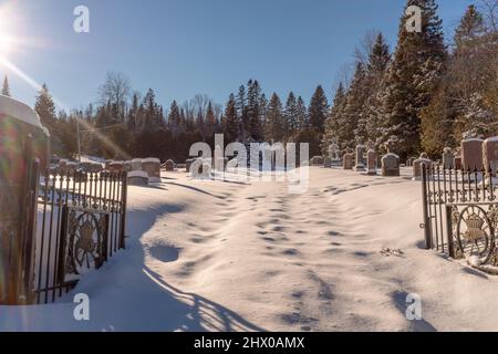 Un cimetière canadien en hiver situé à Saint-Adolph-d'Howard (Québec) avec une croix et des pierres de tête recouvertes de neige, prises par une journée ensoleillée Banque D'Images