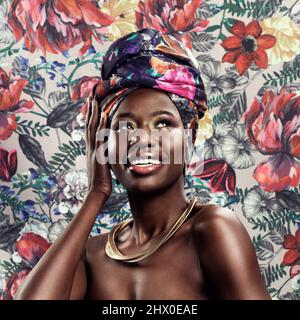 Enveloppez-vous comme le cadeau que vous êtes. Photo studio d'une belle jeune femme portant une tête d'enveloppement africaine traditionnelle sur un fond floral. Banque D'Images