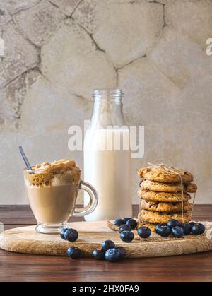 Le café Dalgona dans un verre clair avec des biscuits aux myrtilles et des myrtilles sur une planche de bois. Arrière-plan mural rustique. Café coréen très à la mode. Banque D'Images