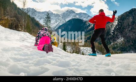 Les enfants apprécient les plaisirs enneigés de l'hiver avec leur père, ayant un combat de boule de neige sur la pente lors d'une journée ensoleillée en montagne. Banque D'Images