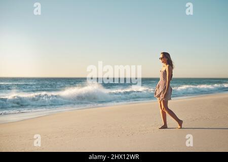 Parfois, la plage est tout ce dont vous avez besoin. Photo d'une jeune femme en train de se promener sur la plage. Banque D'Images