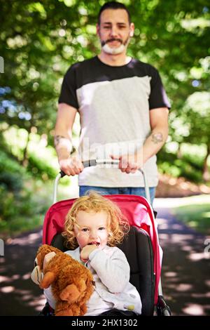 Promenade dans le parc. Portrait d'un père poussant sa petite fille dans une poussette à l'extérieur. Banque D'Images