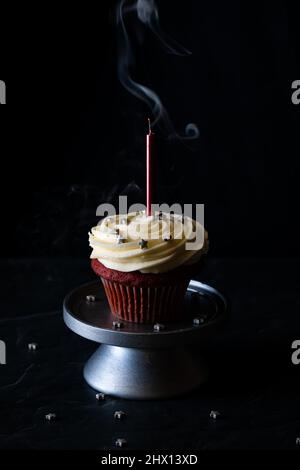 Un cupcake en velours rouge avec de la fumée provenant de la bougie soufflée. Banque D'Images