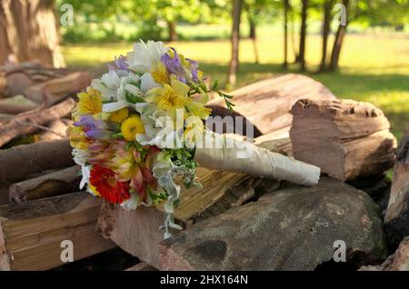 Bouquet de mariage coloré de lilies et de pâquerettes de Gerber sur une pile de bois dans un cadre rural Banque D'Images