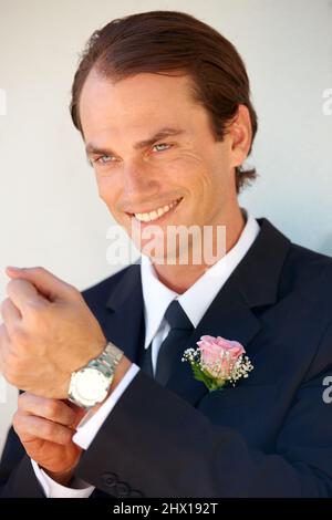 Le grand jour. Un groom heureux ajustant sa montre-bracelet avant la cérémonie de mariage. Banque D'Images