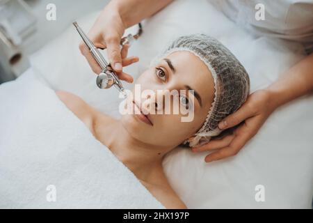 Les femmes font face à la procédure d'oxygénothérapie faciale avec l'appareil. Vue de dessus. Soins de la peau en cosmétologie. Banque D'Images