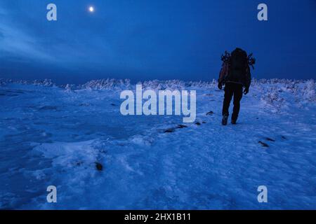 Randonneur sur le sommet du Mont Pierce dans les White Mountains, New Hampshire avant le lever du soleil. La demi-lune est visible en arrière-plan. Banque D'Images