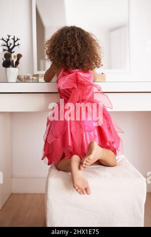 Apprendre les tenants et les aboutissants de la beauté dès le plus jeune âge. Vue arrière d'une petite fille se regardant dans le miroir. Banque D'Images