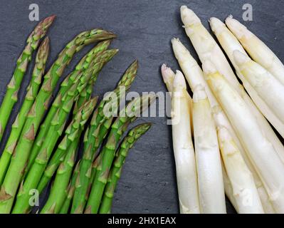 Asperges fraîches vertes et blanches sur fond d'ardoise foncé, comparaison des variétés d'asperges Banque D'Images