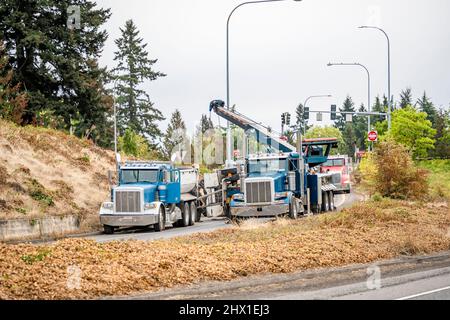 Un semi-camion de remorquage mobile puissant avec flèche allongée fixe un accident de la route essayant de soulever une remorque de camion-benne qui s'est retournée pendant la conduite Banque D'Images