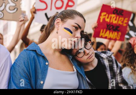 Non à la guerre en Ukraine. Une jeune femme markant contre la guerre avec le drapeau de l'Ukraine peint sur son visage. Groupe de jeunes multiculturels tenant un an Banque D'Images