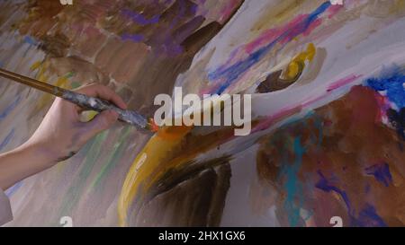 Un artiste designer dessine un aigle sur le mur. Artisan décorateur peint une image avec de l'huile acrylique couleur. Gros plan, magie et obscurité, aspect cinématographique. Peintre peintre vêtu d'un manteau de peinture. Intérieur. Banque D'Images
