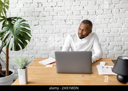 Un homme d'affaires afro-américain sérieux regarde l'écran d'un ordinateur portable, souriant, lisant de bonnes nouvelles. Un homme plein de joie, indépendant ou étudiant, bien fait avec Banque D'Images